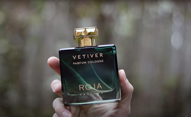 A hand polished bottle of Roja Parfums Vetiver Parfum Cologne held up in one hand.
