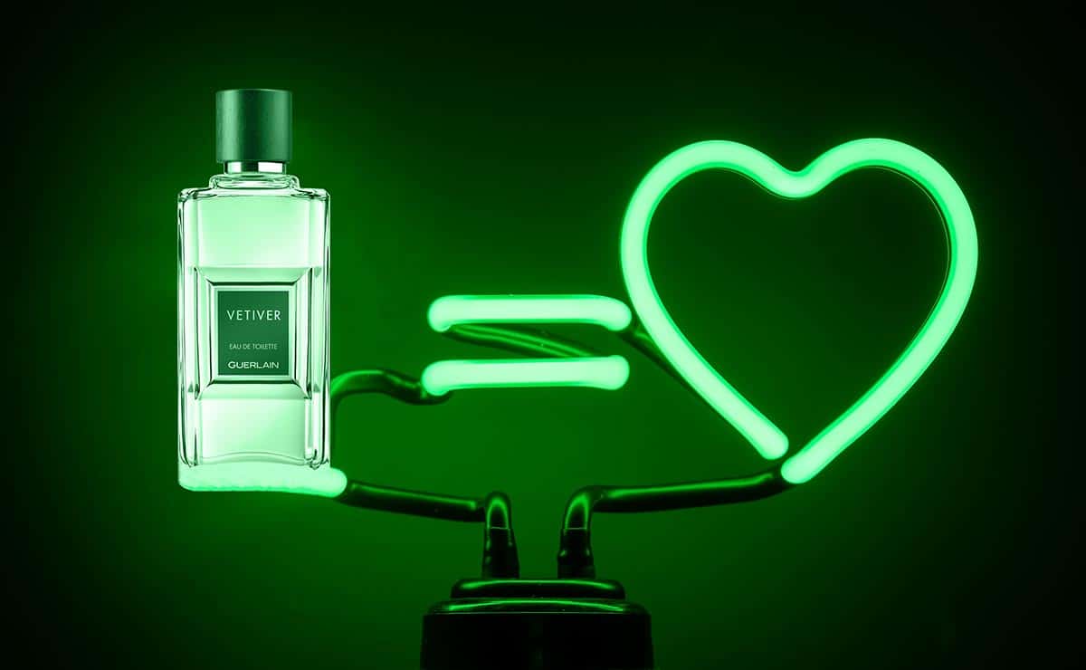 A bottle of Guerlain Vetiver beside a green neon sign of a love heart.