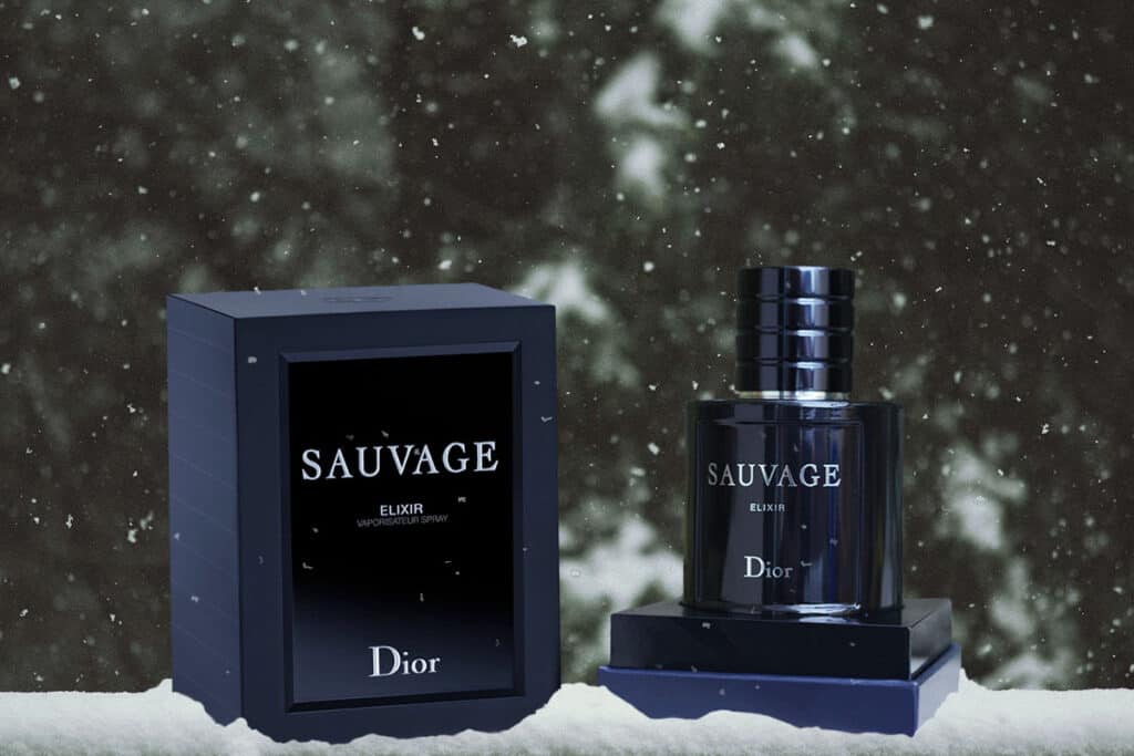 a bottle of dior sauvage elixir sitting in its podium pictured next to its open box, depicted in a winter snowy background.