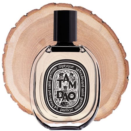 A bottle of Diptyque Tam Dao in front of the fresh cut end face of a wooden log.
