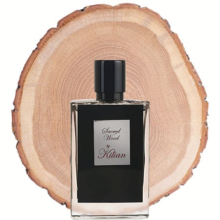 A bottle of Kilian Sacred Wood in front of the fresh cut end face of a wooden log.