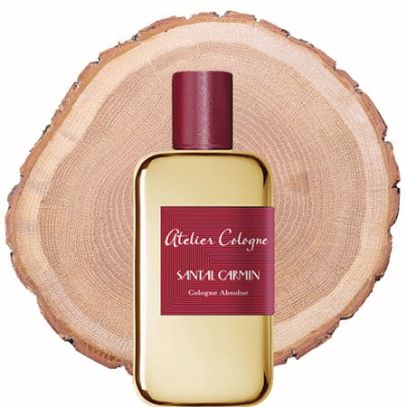 A bottle of Atelier Cologne Santal Carmin in front of the fresh cut end face of a wooden log.