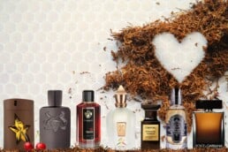 7 different branded tobacco scented cologne bottles lined up alongside some pipe tobacco that is shaped like a heart with a honeycomb background.