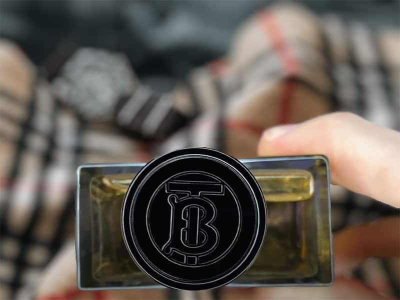 A bottle of Burberry Hero EDT in the hand showing a close-up of the brand’s TB logo embossed on the top of the bottle’s cap.