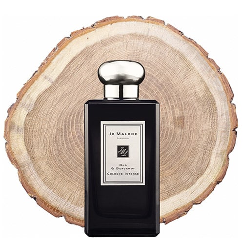 A bottle of Jo Malone Oud and Bergamot in front of the fresh cut end face of an oud wooden log.