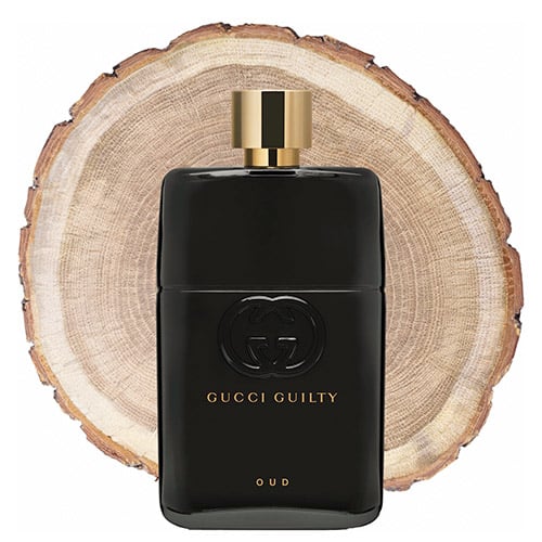 A bottle of Gucci Guilty Oud in front of the fresh cut end face of an oud wooden log.