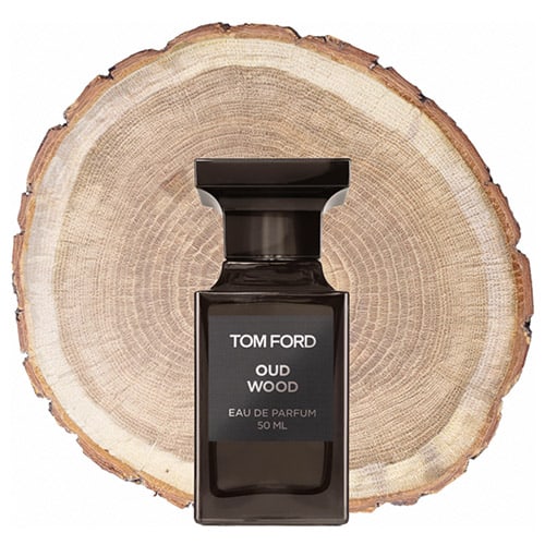 A bottle of Tom Ford Oud Wood in front of the fresh cut end face of an oud wooden log.