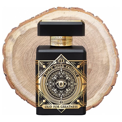 A bottle of Initio Parfums Prives Oud for Greatness in front of the fresh cut end face of an oud wooden log.