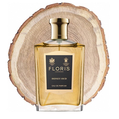 A bottle of Floris Honey Oud in front of the fresh cut end face of an oud wooden log.
