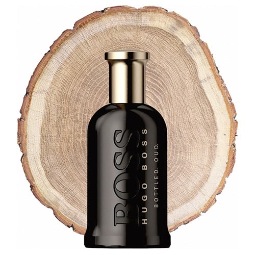 A bottle of Hugo Boss Bottled Oud in front of the fresh cut end face of an oud wooden log.