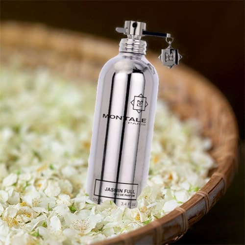 A bottle of Montale Jasmin Full resting on a bed of jasmine flowers in a round woven basket.