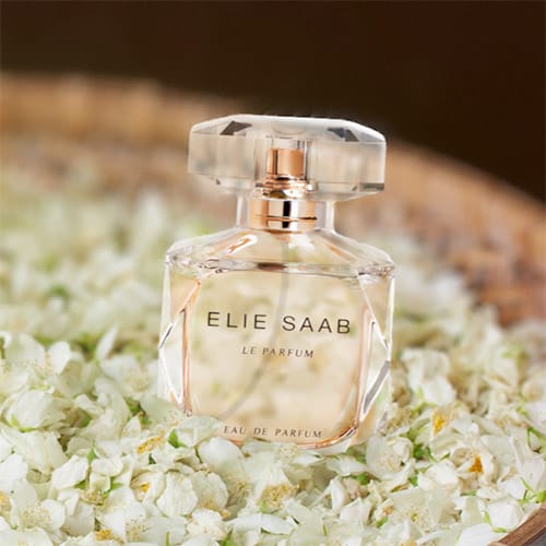 A bottle of Elie Saab Le Parfum resting on a bed of jasmine flowers in a round woven basket.