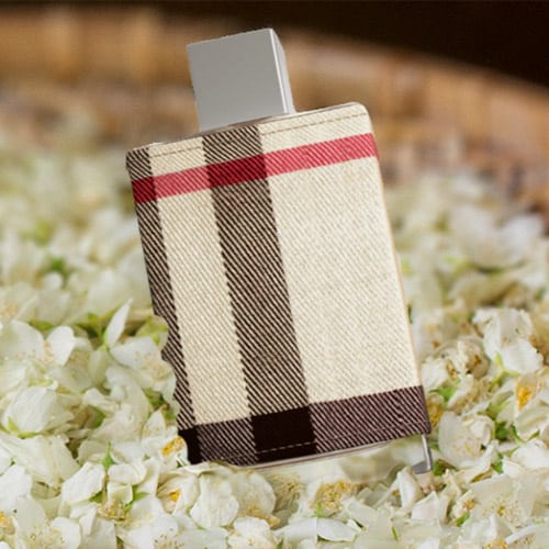 A bottle of Burberry London for women resting on a bed of jasmine flowers in a round woven basket.