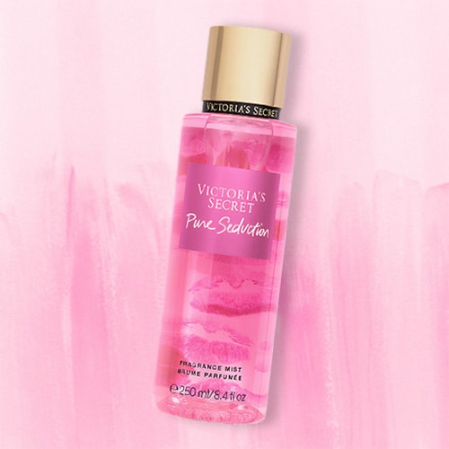 A bottle of Victoria’s Secret Pure Seduction Body Mist lying flat on top of a striped light pink colored table.