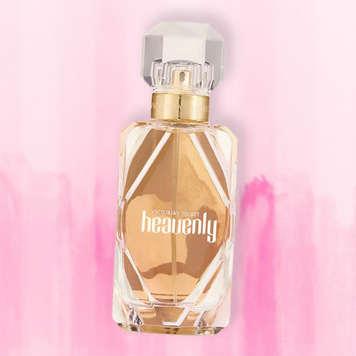 A bottle of Victoria’s Secret Heavenly EDP lying flat on top of a striped light pink colored table.