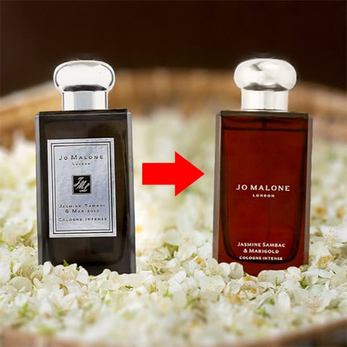 An old-style bottle of Jo Malone Jasmine Sambac & Marigold next to the new style bottle of the same scent. Both bottles are resting on a bed of jasmine flowers in a round woven basket. A red arrow points from the old-style bottle, on the left, to the new style bottle, on the right.