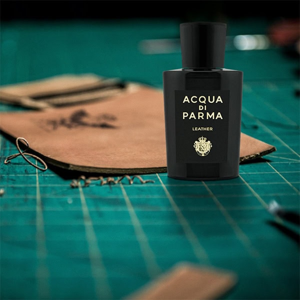 A closeup of a bottle of Acqua Di Parma Leather on a leather cutting board next to a piece of freshly cut leather.