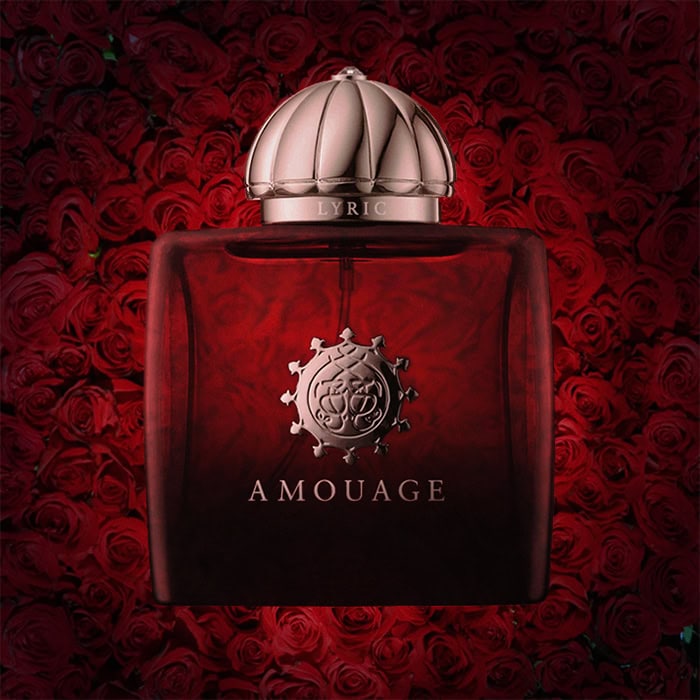 A close-up of an illuminated bottle of Amouage Lyric Woman with a dense wall of dark red roses in the background.