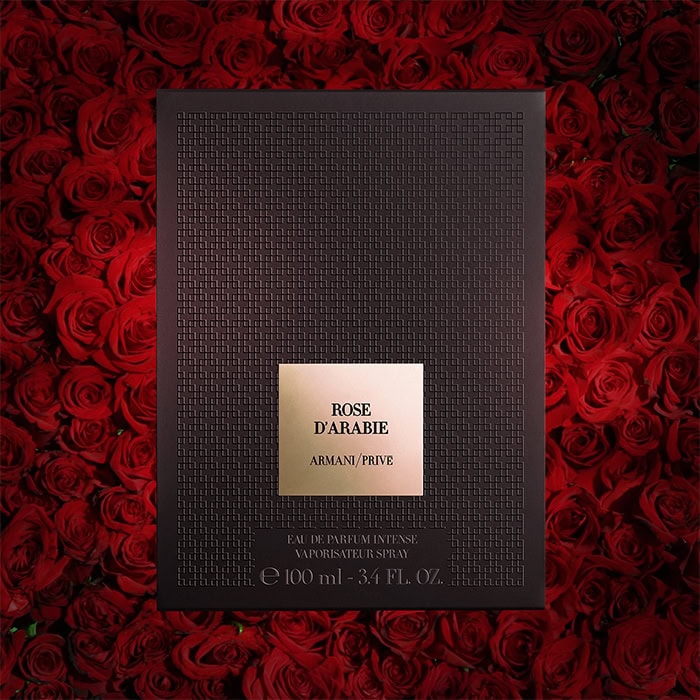 A close-up of Armani Prive Rose D’Arabie’s presentation box. The box is illuminated with a dense wall of dark red roses in the background.