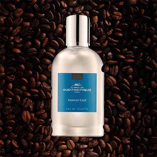 A bottle of Comptoir Sud Pacifique Vanille Café placed faceup on top of a pile of dark roasted coffee beans.