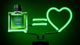 A glowing neon-green bottle of Guerlain’s Vetiver De Guerlain EDP next to a glowing neon-green lamp that is in the shape of a love-heart symbol.