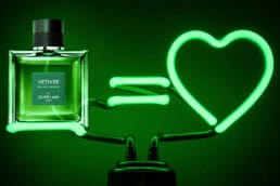 A glowing neon-green bottle of Guerlain’s Vetiver De Guerlain EDP next to a glowing neon-green lamp that is in the shape of a love-heart symbol.