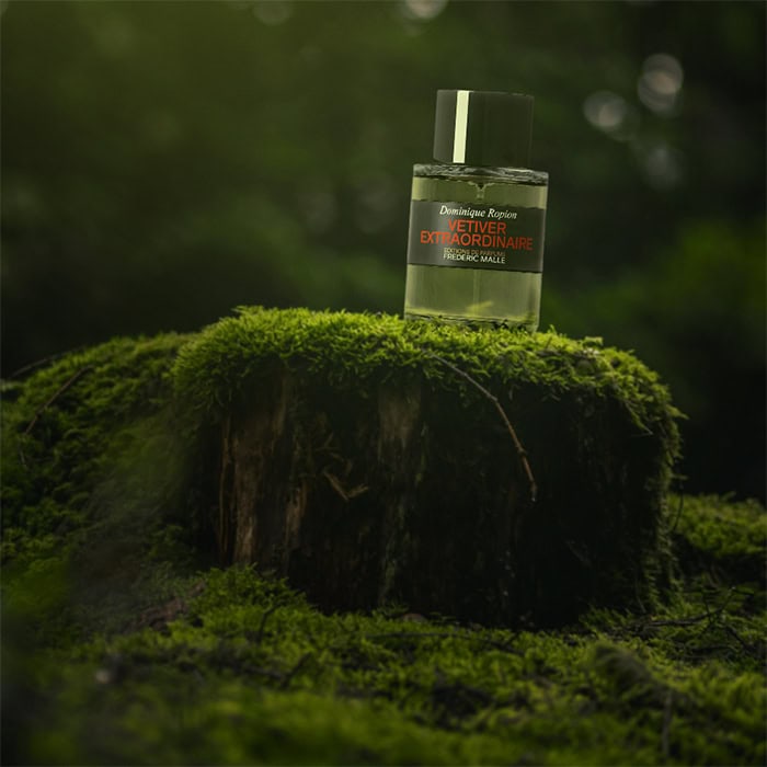 A close-up of a bottle of Editions de Parfums Frederic Malle Vetiver Extraordinaire sitting on top of an old green moss-covered tree stump in the forest.