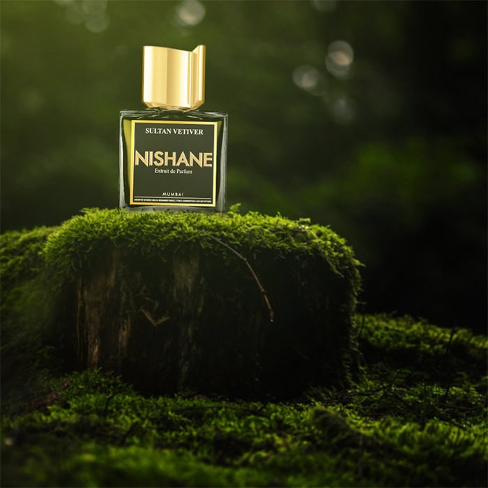 A close-up of a bottle of Nishane Sultan Vetiver sitting on top of an old green moss-covered tree stump in the forest.