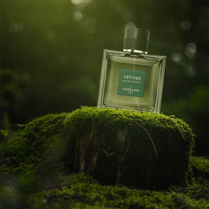 A close-up of a bottle of Guerlain’s Vetiver De Guerlain sitting on top of an old green moss-covered tree stump in the forest.