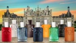 A close-up of the presentation bottles from a selection of 9 of the best Parfums de Marly fragrances. The bottles are lined up on the ground in 2 rows with a chateau in the background.