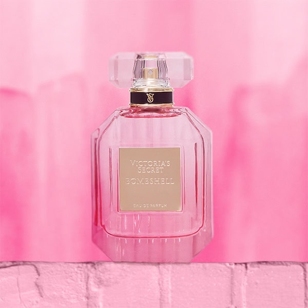 A close-up of the new, updated Victoria’s Secret Bombshell EDP bottle. The bottle is sitting on top of a light pink colored brick wall.