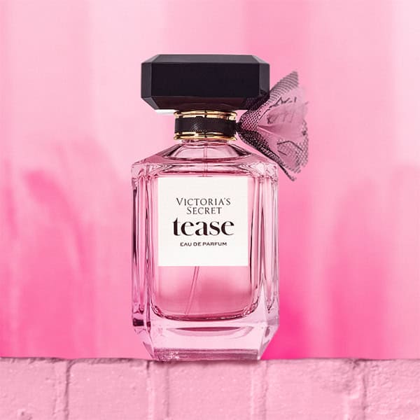 A close-up of a Victoria’s Secret Tease EDP bottle. The bottle is sitting on top of a light pink colored brick wall.