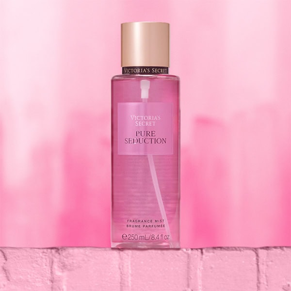 A close-up of the new, updated Victoria’s Secret Pure Seduction Body Mist bottle. The bottle is sitting on top of a light pink colored brick wall.