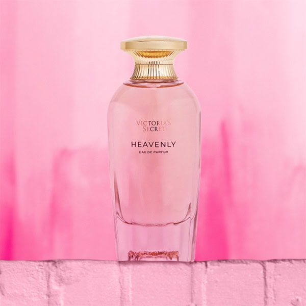 A close-up of the new, updated Victoria’s Secret Heavenly EDP bottle. The bottle is sitting on top of a light pink colored brick wall.
