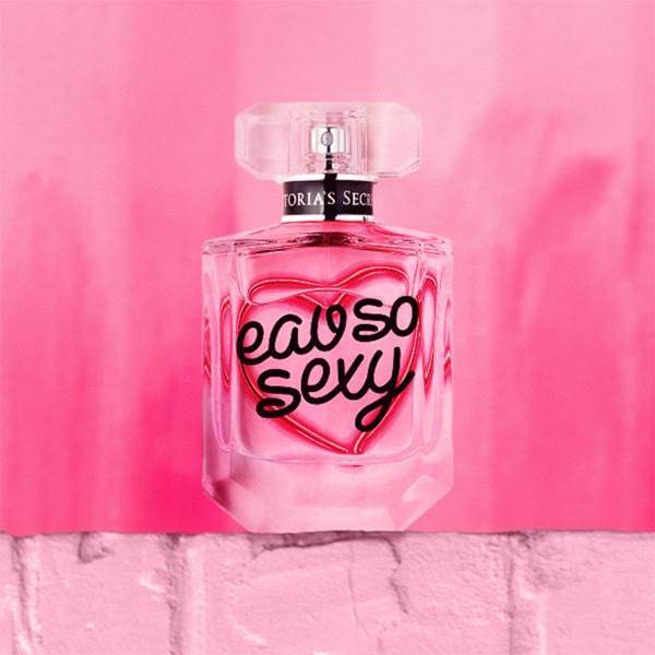 A close-up of a Victoria’s Secret Eau So Sexy EDP bottle. The bottle is sitting on top of a light pink colored brick wall.