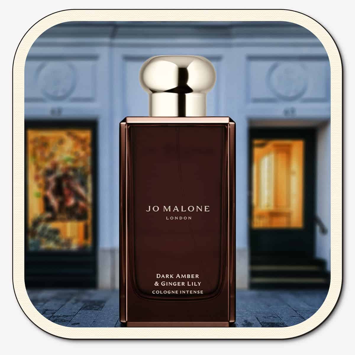 A close-up of the front face of a bottle of Jo Malone Dark Amber & Ginger Lily Cologne Intense. The bottle is placed on the ground with the Jo Malone global flagship storefront in 
London in the background.
