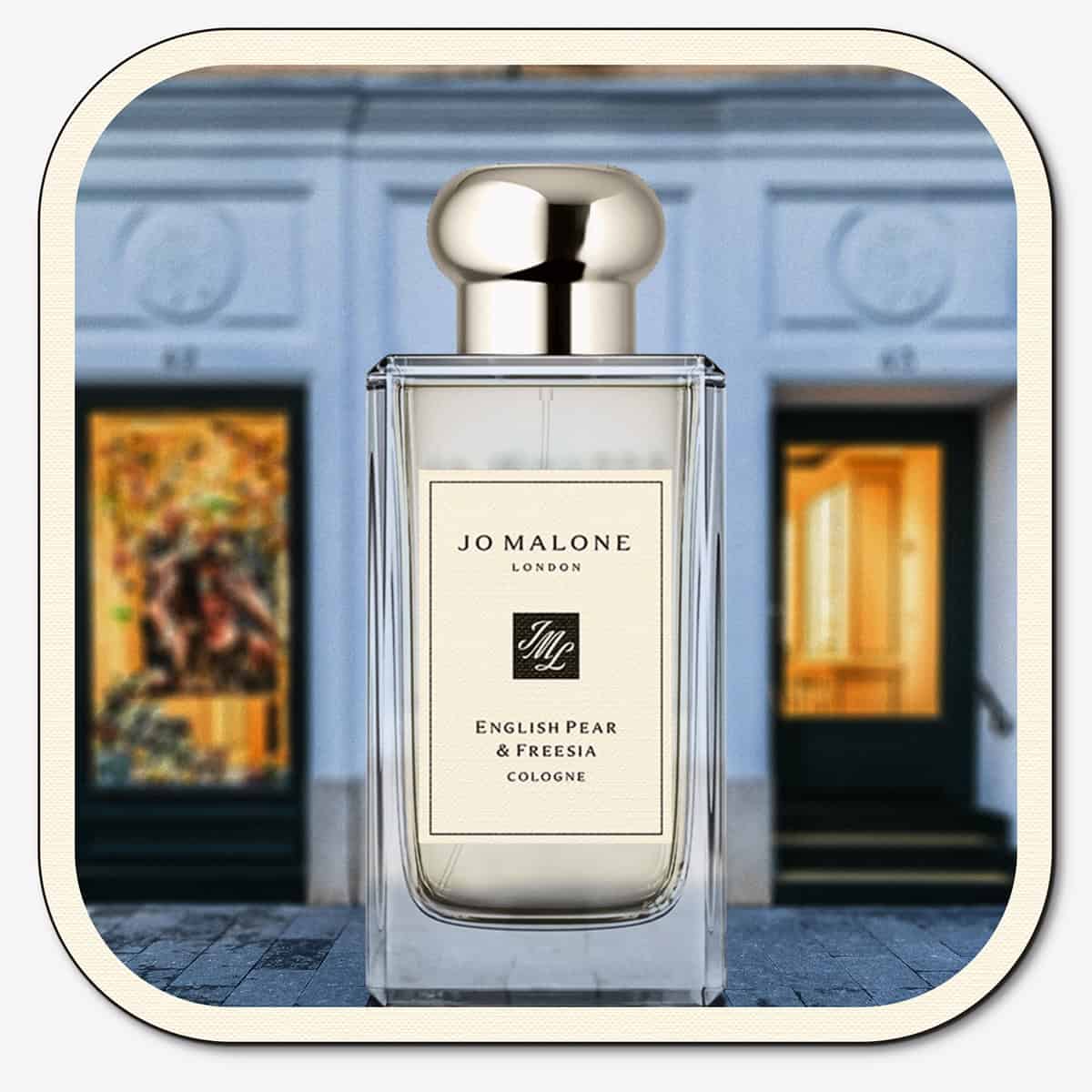 A close-up of the front face of a bottle of Jo Malone English Pear & Freesia Cologne. The bottle is placed on the ground with the Jo Malone global flagship storefront in 
London in the background.
