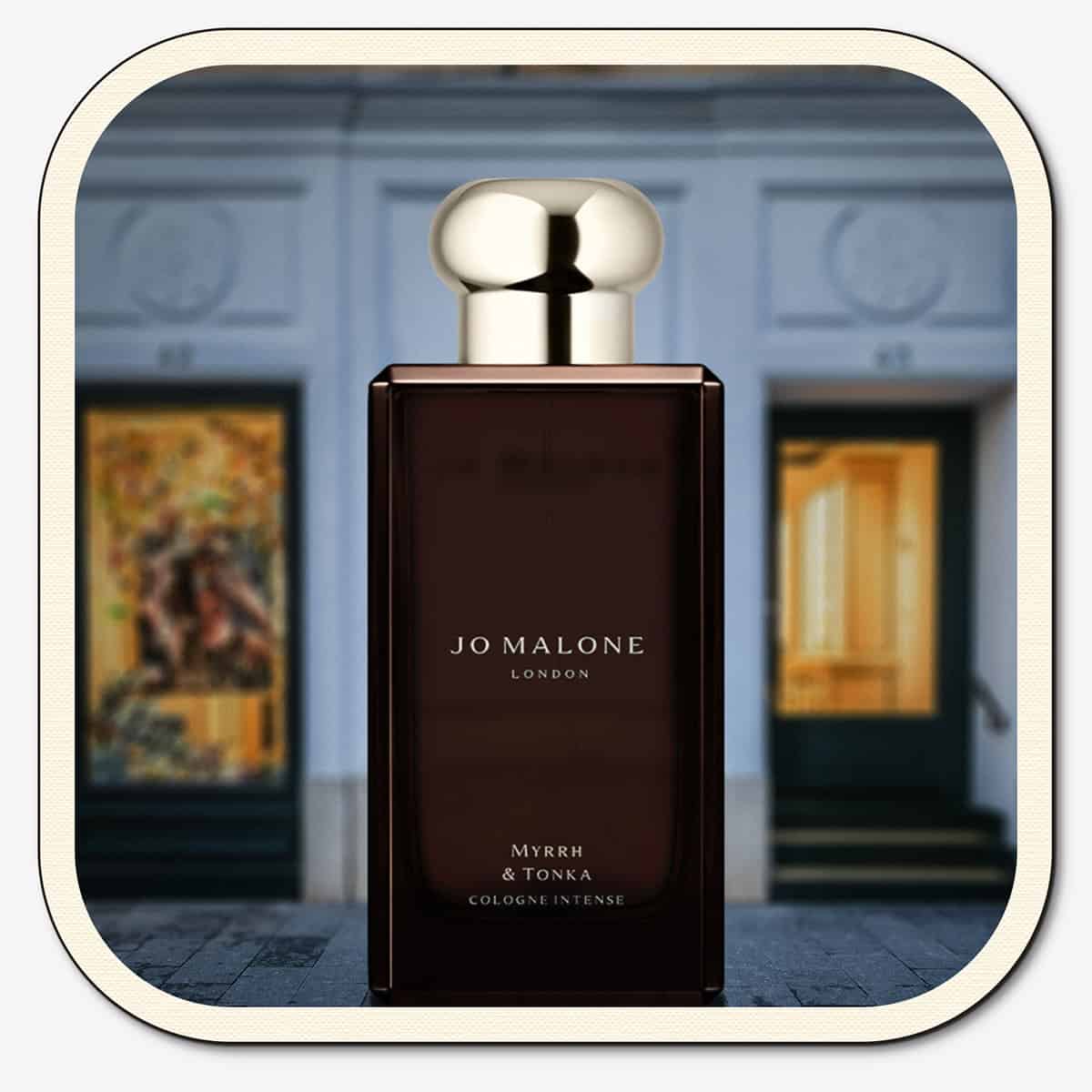 A close-up of the front face of a bottle of Jo Malone Myrrh & Tonka Cologne Intense. The bottle is placed on the ground with the Jo Malone global flagship storefront in 
London in the background.