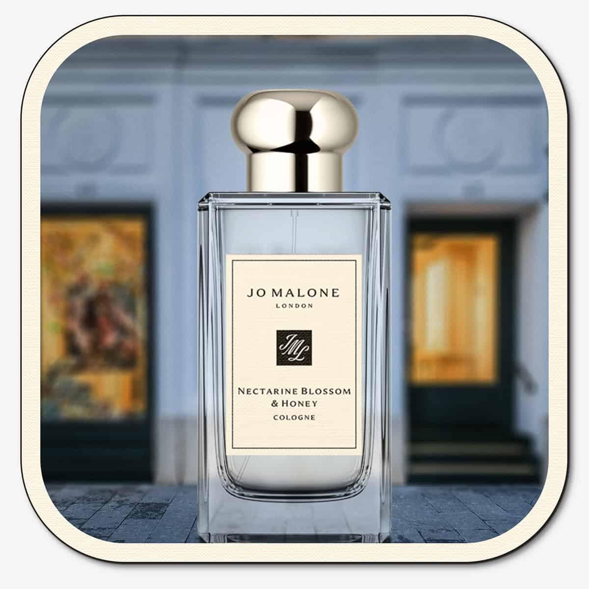 A close-up of the front face of a bottle of Jo Malone Nectarine Blossom & Honey Cologne. The bottle is placed on the ground with the Jo Malone global flagship storefront in 
London in the background.