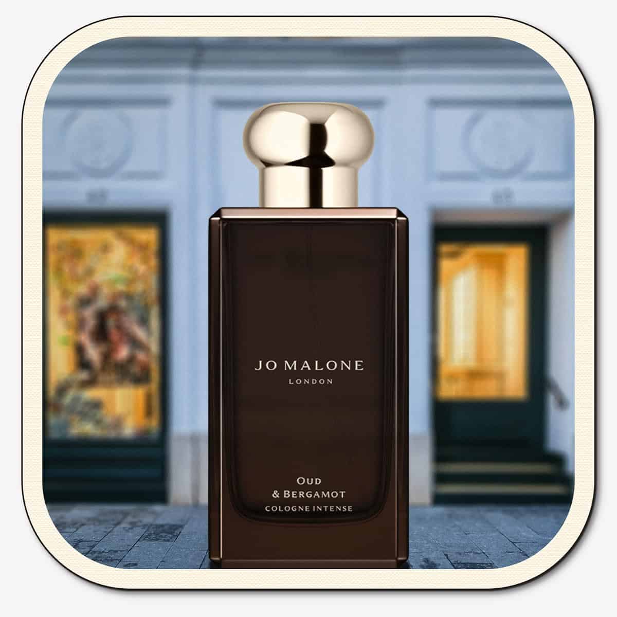 A close-up of the front face of a bottle of Jo Malone Oud & Bergamot Cologne Intense. The bottle is placed on the ground with the Jo Malone global flagship storefront in 
London in the background.