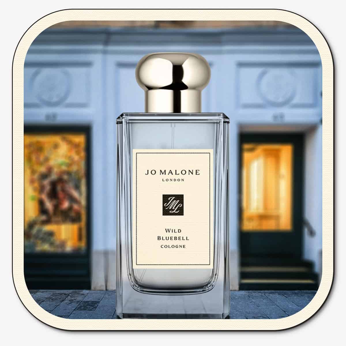 A close-up of the front face of a bottle of Jo Malone Wild Bluebell Cologne. The bottle is placed on the ground with the Jo Malone global flagship storefront in 
London in the background.