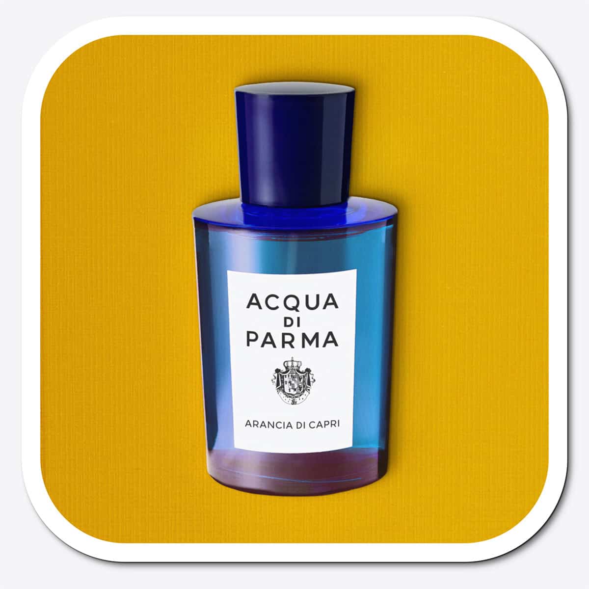 A close-up of the front face of a bottle of Acqua Di Parma Arancia Di Capri. The bottle is placed on its side, label side up, and is resting on a yellow-colored textured surface.