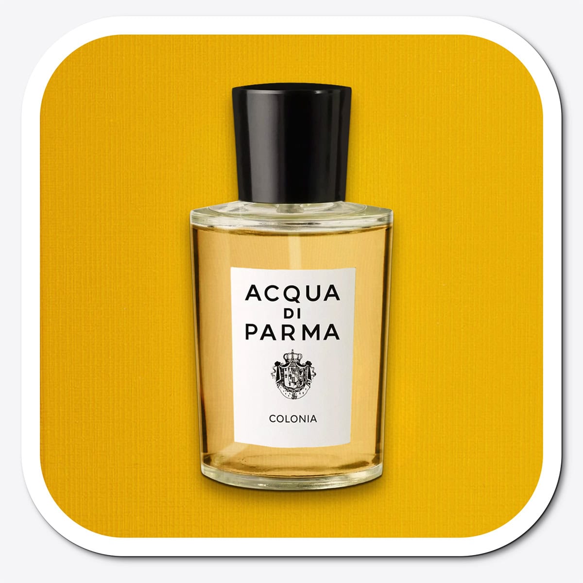 A close-up of the front face of a bottle of Acqua Di Parma Colonia. The bottle is placed on its side, label side up, and is resting on a yellow-colored textured surface.