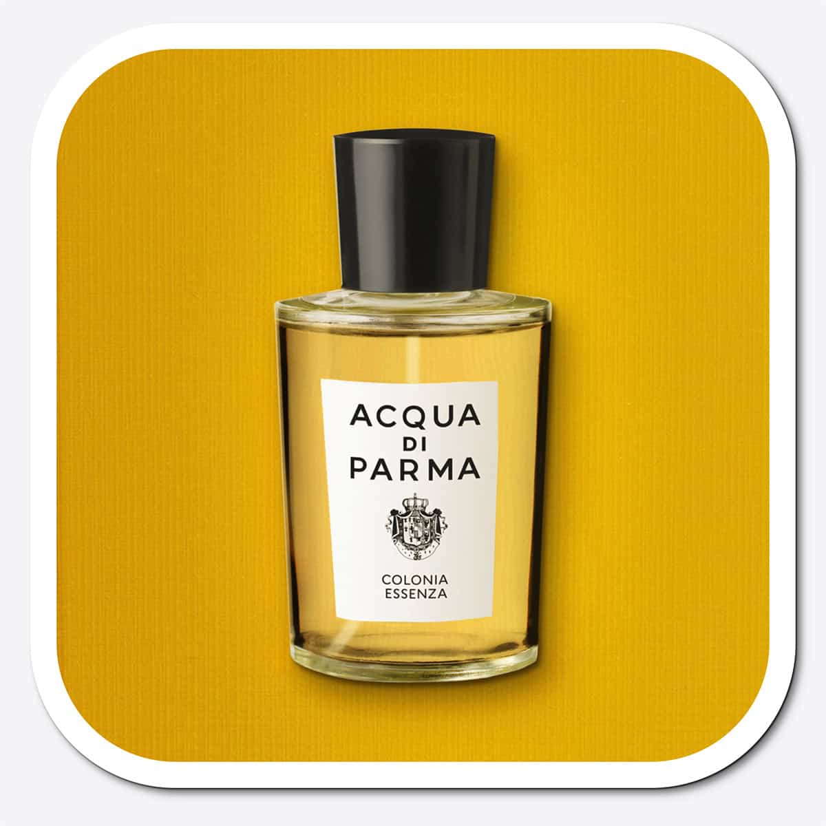 A close-up of the front face of a bottle of Acqua Di Parma Colonia Essenza. The bottle is placed on its side, label side up, and is resting on a yellow-colored textured surface.