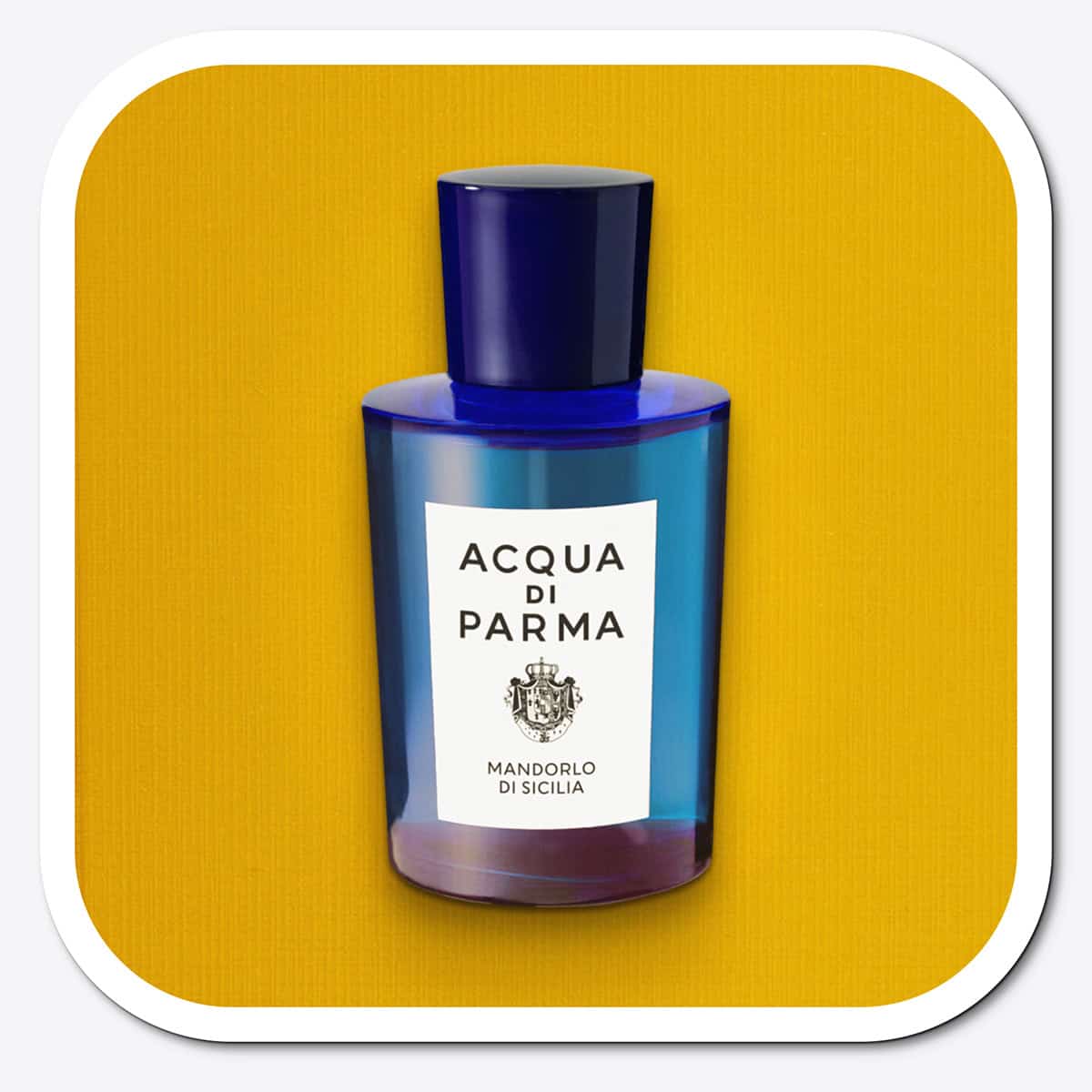 A close-up of the front face of a bottle of Acqua Di Parma Mandorlo Di Sicilia. The bottle is placed on its side, label side up, and is resting on a yellow-colored textured surface.